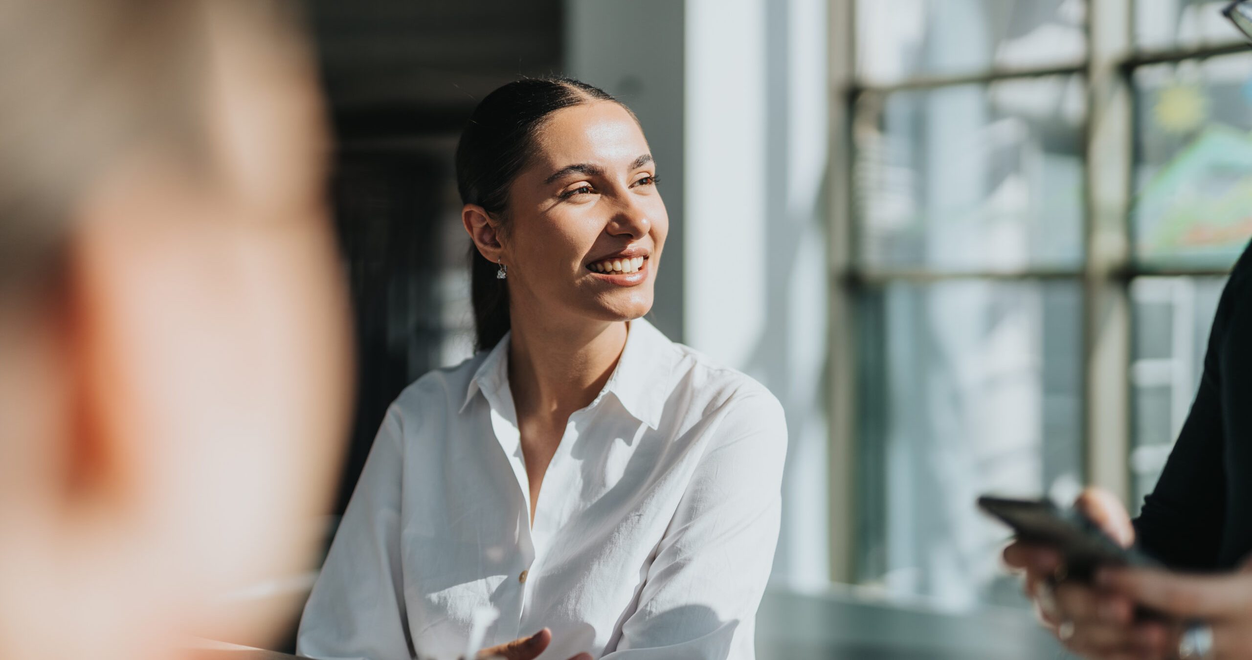 A cheerful businesswoman in a white shirt enjoys a conversation in a bright office kitchen, fostering a welcoming and collaborative atmosphere. Ideal for business, teamwork, and professional interaction themes.
