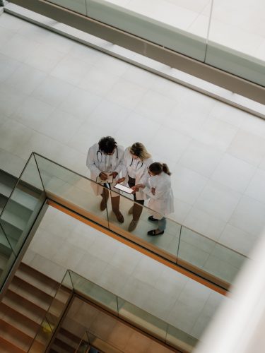 Doctors using digital tablet, collaborating on patient care in modern hospital atrium, enhancing healthcare with technology